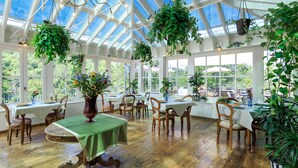 A sunroom with wooden flooring, tables with green tablecloths, and hanging plants. - Le Lappe (Cavriglia)