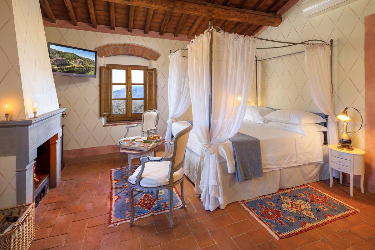 Un dormitorio con cama, una silla, una mesa con comida, una chimenea y un televisor.