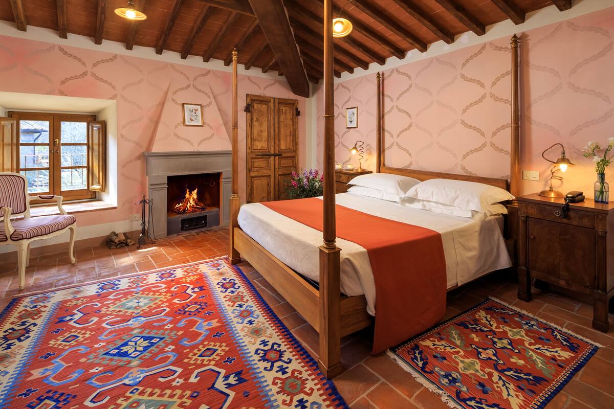 Un dormitorio tradicional con cama con dosel, chimenea y un ventanal grande.
