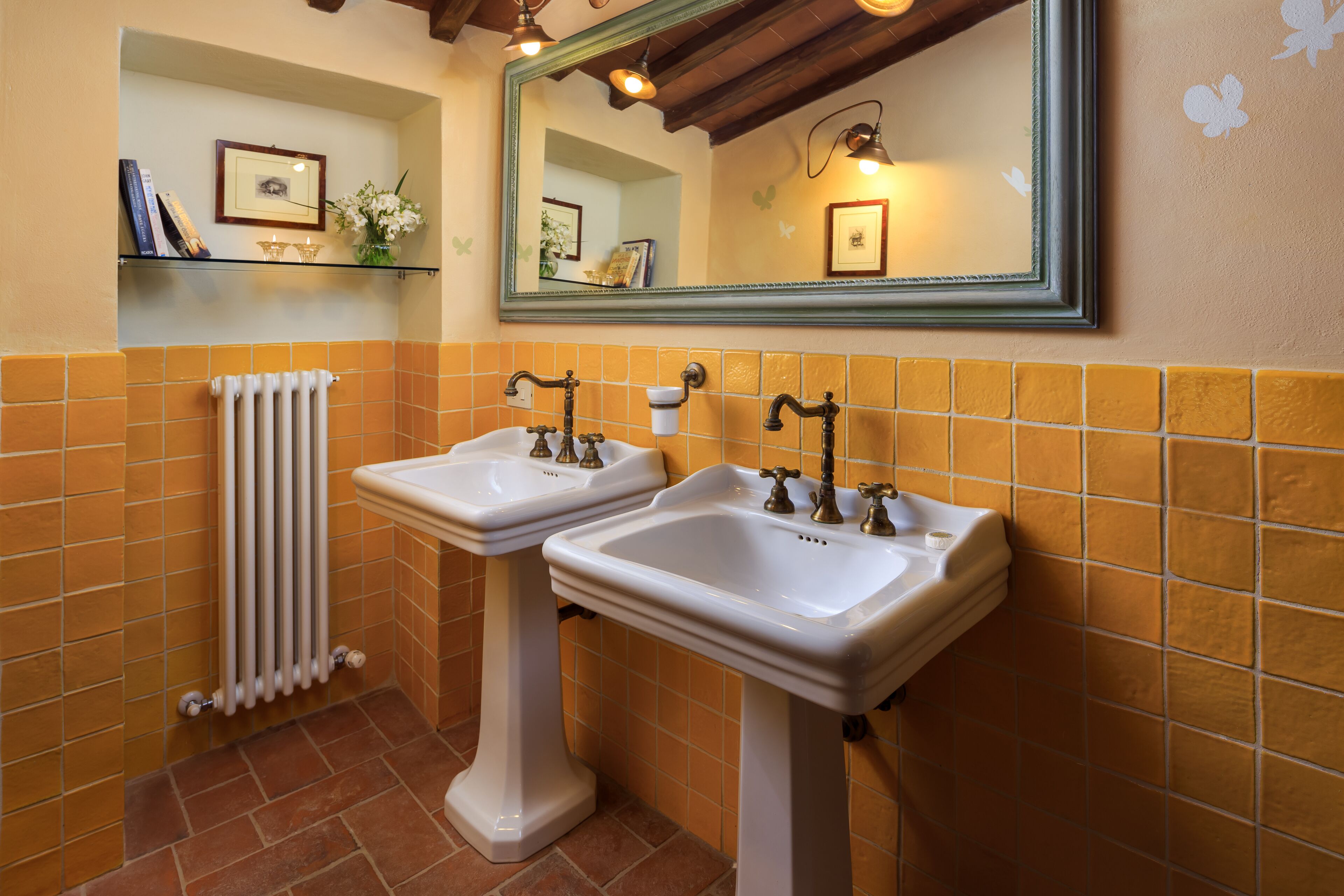 A bathroom with two white pedestal sinks, a mirror, and a radiator.