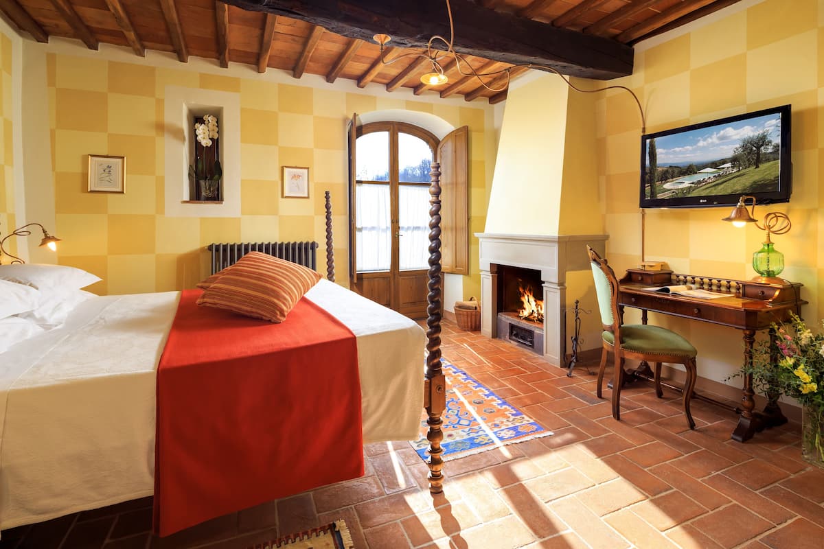 Un dormitorio con cama, escritorio, silla, chimenea y televisor.