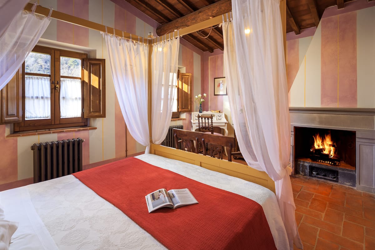 Un dormitorio con cama, chimenea y ventana con cortinas.