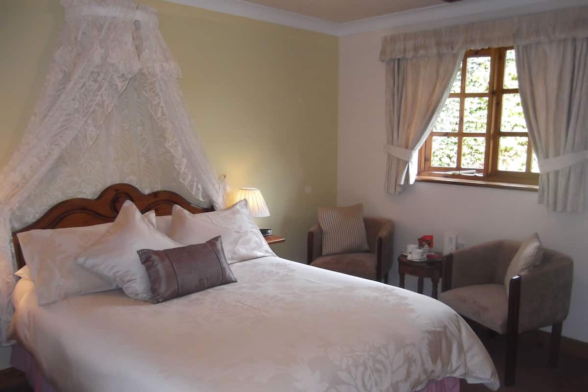 Une chambre à coucher avec un lit à baldaquin, une chaise, une table de chevet avec une lampe et une fenêtre avec des rideaux.