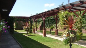 Un área de patio techada con un muro de ladrillo, un sendero de piedra y plantas en macetas.