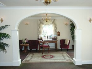 A formal dining area with a chandelier, red upholstered chairs, a wooden table, and a patterned rug. - Brandon Lodge (Hereford)