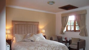 Un dormitorio con una cama grande, dos lámparas de noche, una silla, una mesita y un ventanal con cortinas.