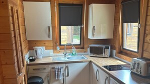 Cocina compacta con paredes de madera, un lavamanos, un hervidor, un microondas y un tostador.