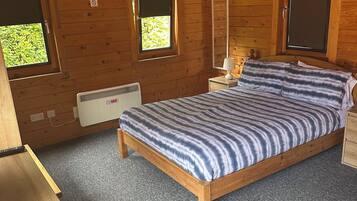 Une chambre dans une cabane en bois, avec un lit, deux fenêtres, un radiateur et une table de chevet.