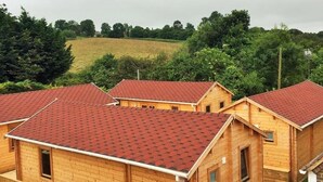 Un hilera de cabañas de madera con techos rojos, rodeadas por una valla de madera, con un fondo de campos verdes y árboles.