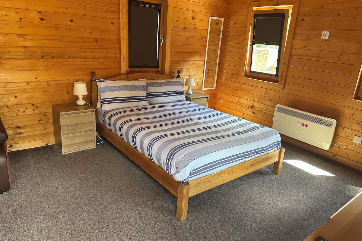 A wooden cabin bedroom with a bed, nightstands, a mirror, and a window.