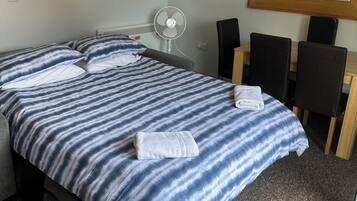 Et hotelværelse med seng, skrivebord, stol, ventilator og spejl.