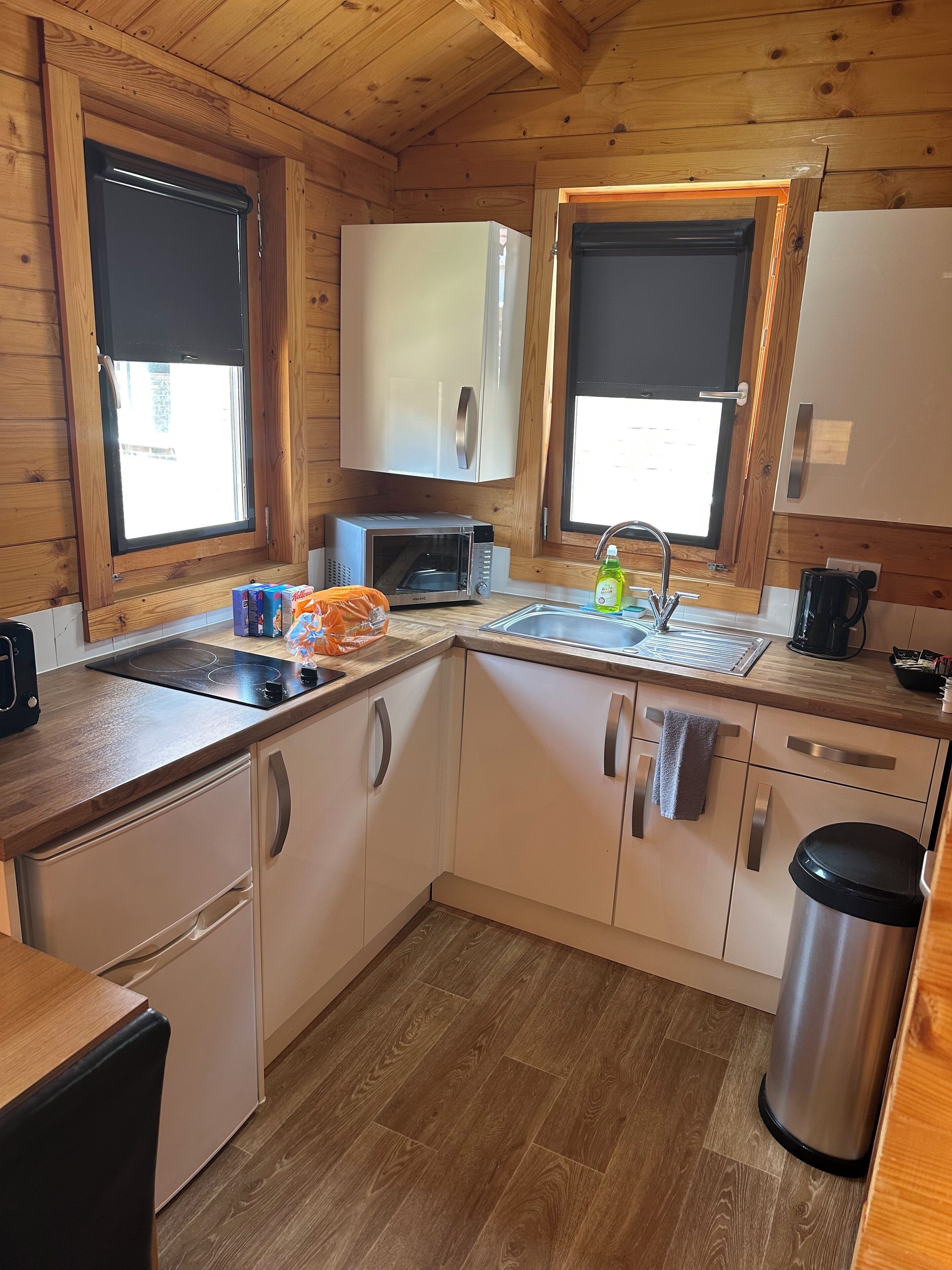 A compact kitchen with wooden walls, a microwave, a sink, and cabinets.