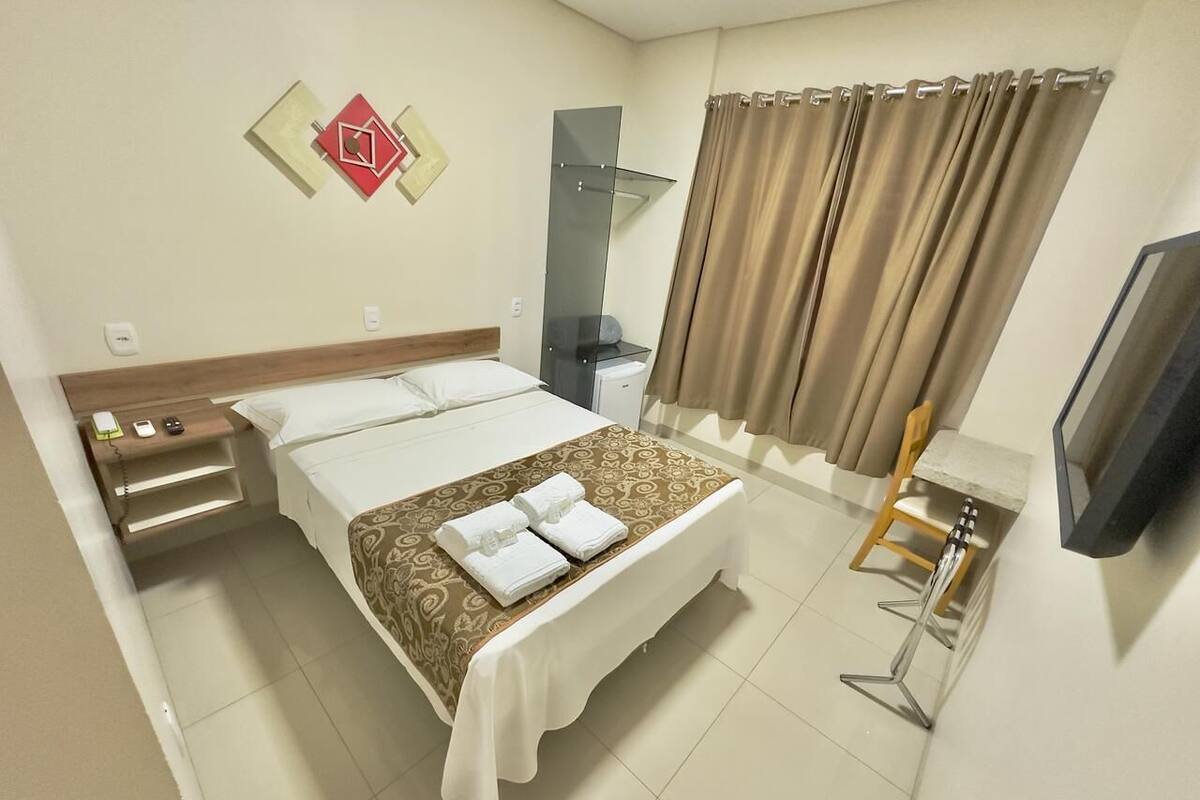 Habitación de hotel con cama, mesita de noche, televisor y una pequeña mesa con una silla.