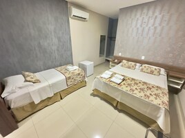 Habitación de hotel con dos camas, una mesita de noche pequeña, aire acondicionado de pared y un espejo.