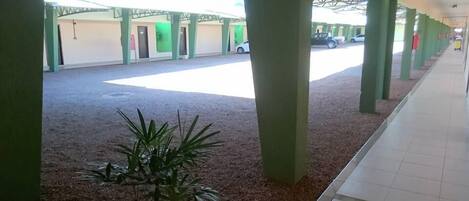 Un espacio al aire libre techado con pilares verdes, piso de baldosas y una planta en primer plano.