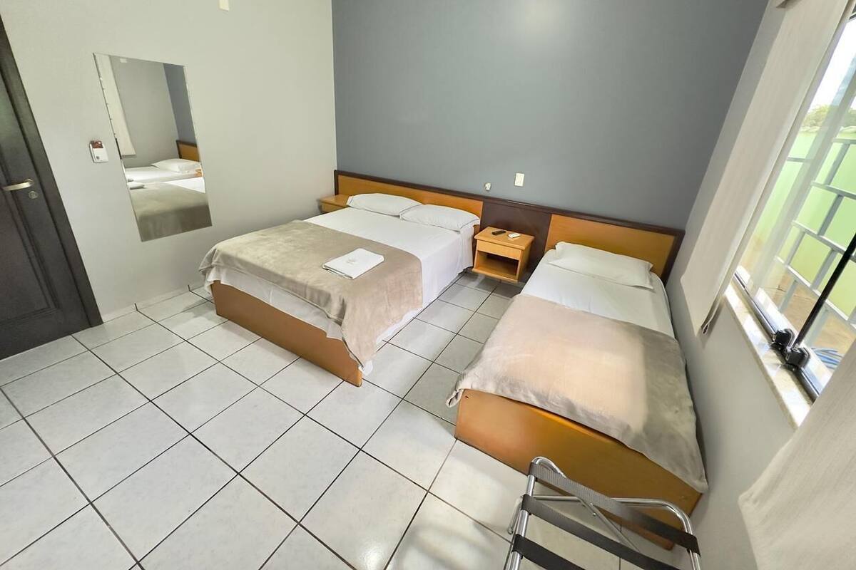 Una habitación de hotel con dos camas, una mesita de noche pequeña, un espejo y una ventana.