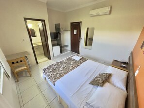 A hotel room with a bed, a wooden chair, a desk, and a mirror.
