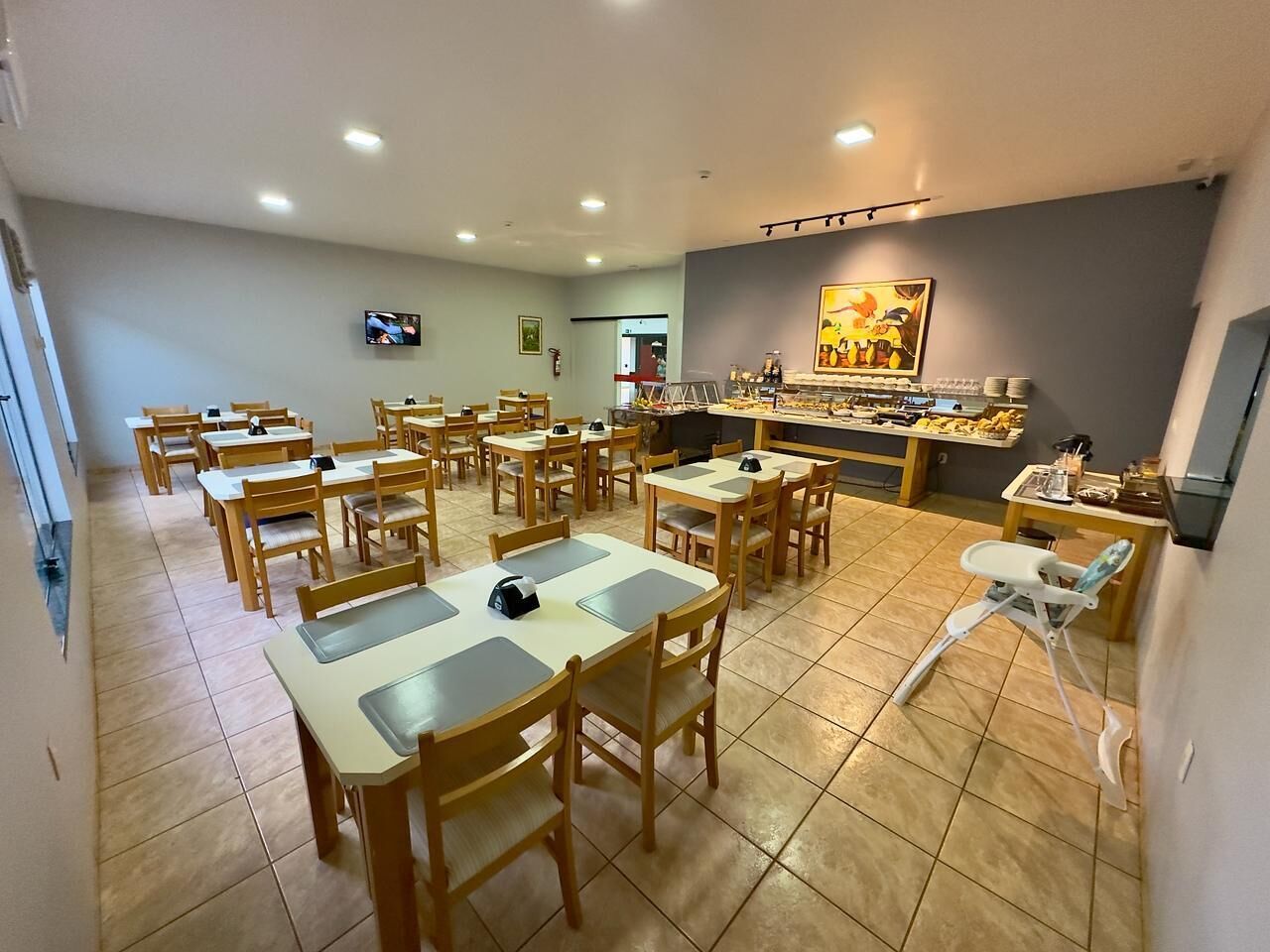Un comedor con varias mesas y sillas, un televisor montado en la pared y una barra con diversos objetos.