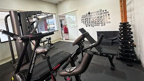A gym with cardio equipment, weightlifting benches, and dumbbells. - Hotel Pousada Real (Sinop)