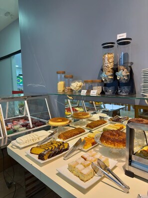 A buffet with various food items, including cakes and pastries, displayed on a glass counter. - Hotel Pousada Real (Sinop)