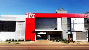A commercial building with a red and white facade, featuring a large garage door and a sign that reads "POUSADA REAL". - Hotel Pousada Real (Sinop)