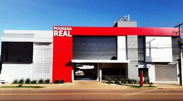 Edificio comercial con fachada roja y blanca, que presenta un amplio portón de garaje y un letrero que dice "POUSADA REAL".