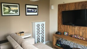 A living room with a beige sofa, a white cabinet with glass doors, a mounted TV, and two framed pictures on the wall.