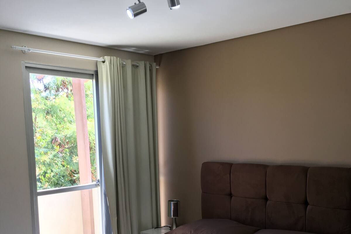 Une chambre à coucher avec un grand lit, une table de chevet, une lampe et une fenêtre avec des rideaux.