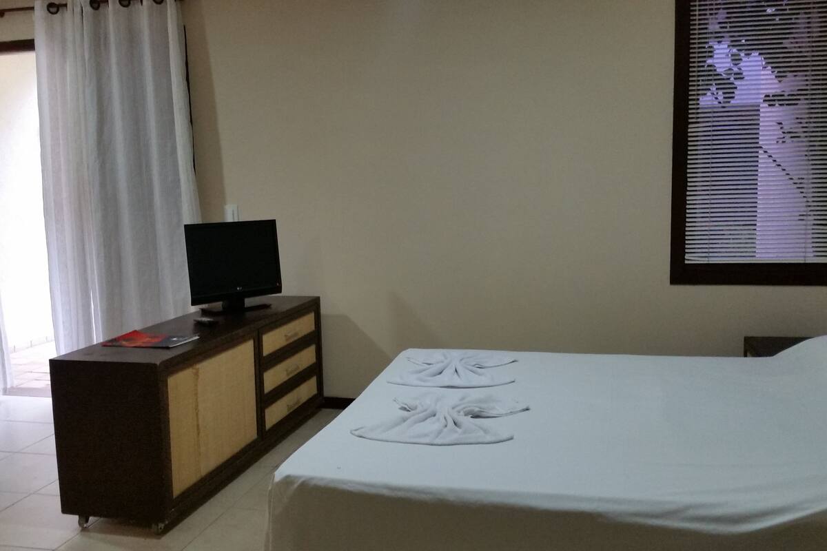 A hotel room with a bed, a dresser, a television, and a window with blinds.