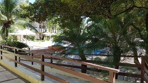 A wooden staircase leading to a pool area with palm trees and umbrellas. - Solar Pipa Apartamentos (Tibau do Sul)