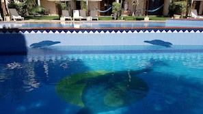 A swimming pool with clear water, lounge chairs, and a tiled edge.
