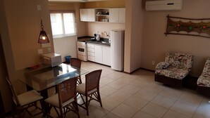 A compact kitchen with white cabinets, a dining table with chairs, and a small sofa. - Solar Pipa Apartamentos (Tibau do Sul)