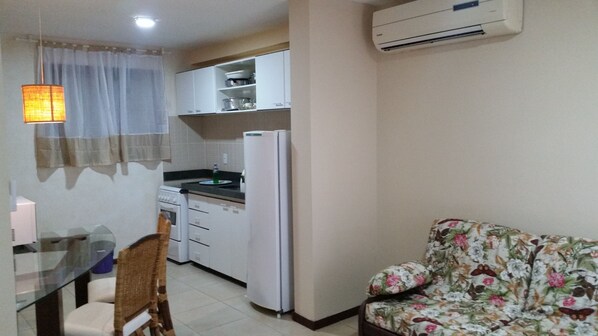 A compact kitchen with white cabinets, a refrigerator, and a dining area with a table and chairs. - Solar Pipa Apartamentos (Tibau do Sul)