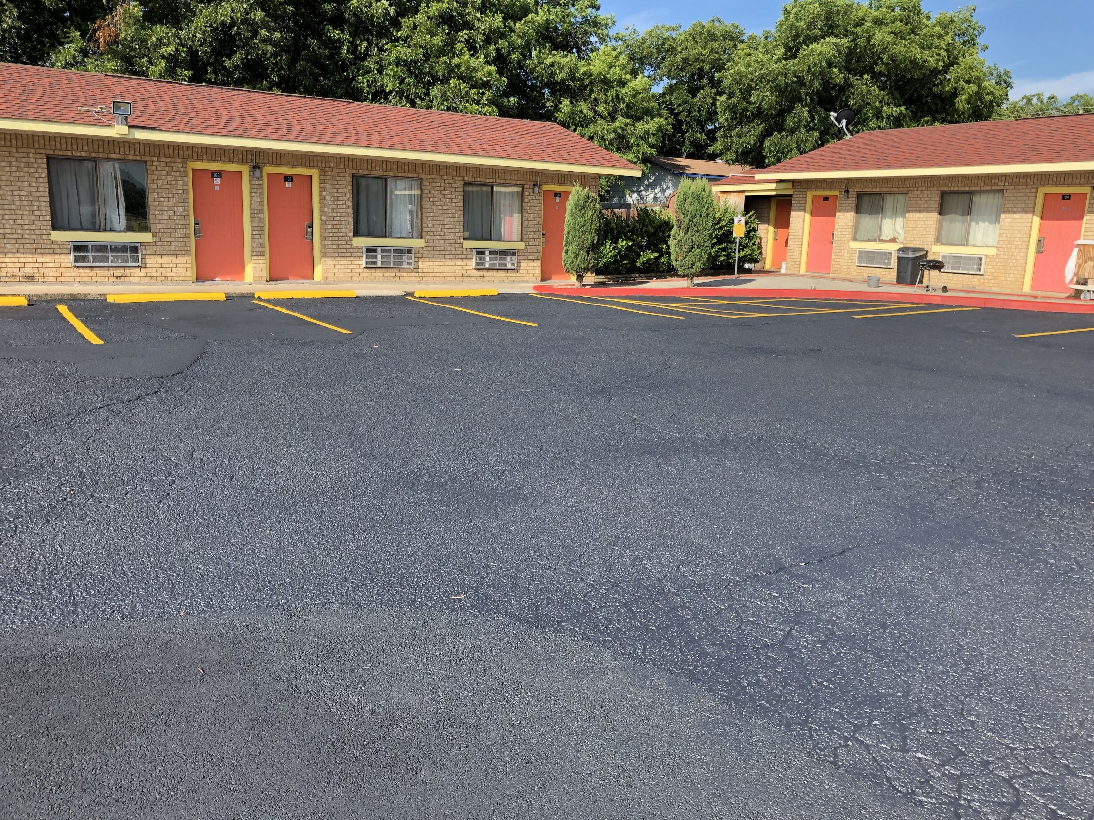 Un motel con edificios de dos pisos, cada uno con una puerta roja y varias ventanas. El estacionamiento está delimitado con líneas amarillas.