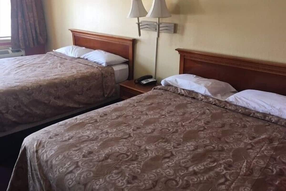Duas camas com roupa de cama estampada, uma mesinha de cabeceira com abajur e um telefone sobre a mesa.