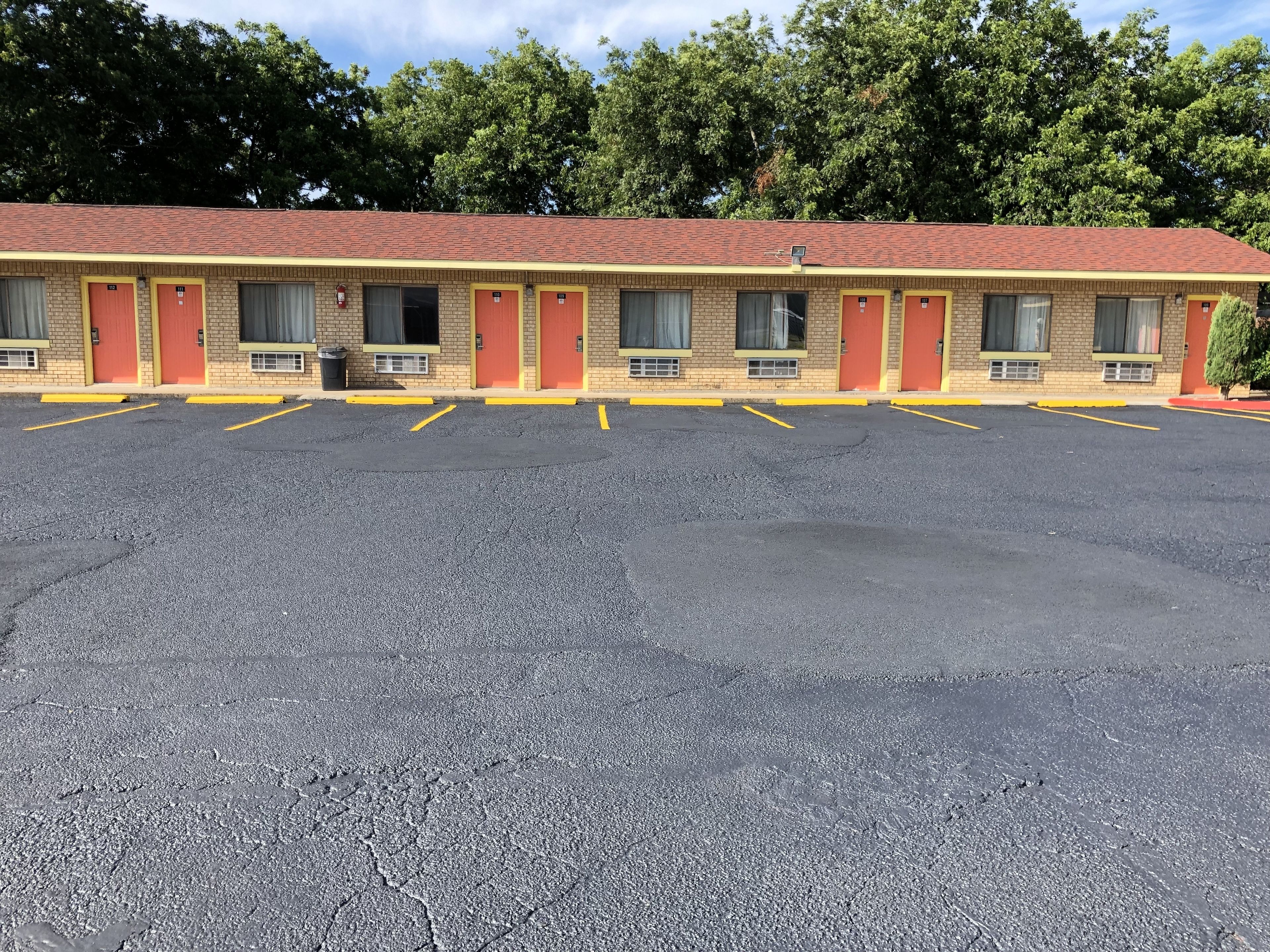 Un motel à la façade en briques, aux bordures jaunes et aux portes rouges. Il dispose d’un grand parking avec des places délimitées.