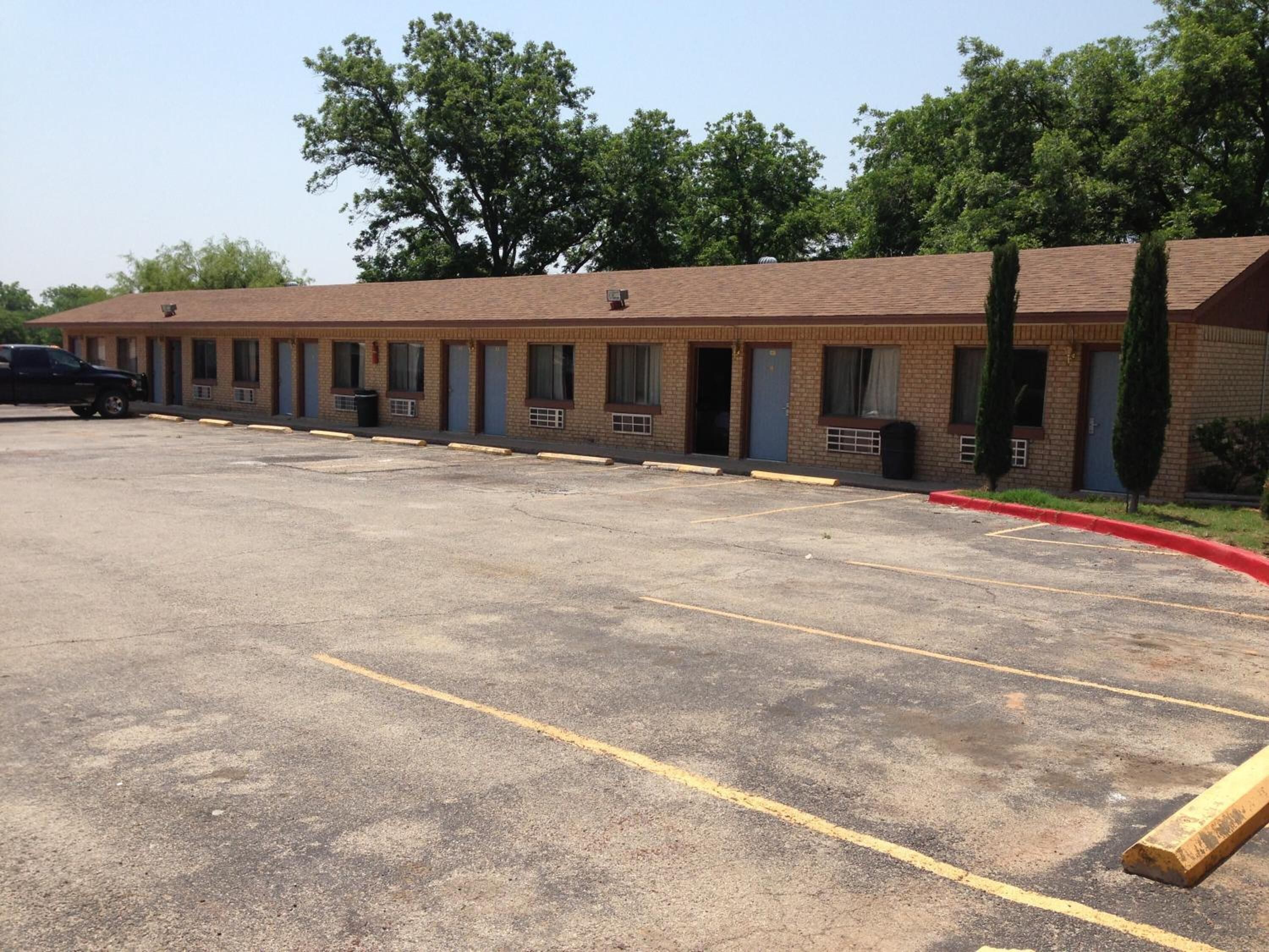 A motel with a row of rooms, a parking lot, and a small garden area.