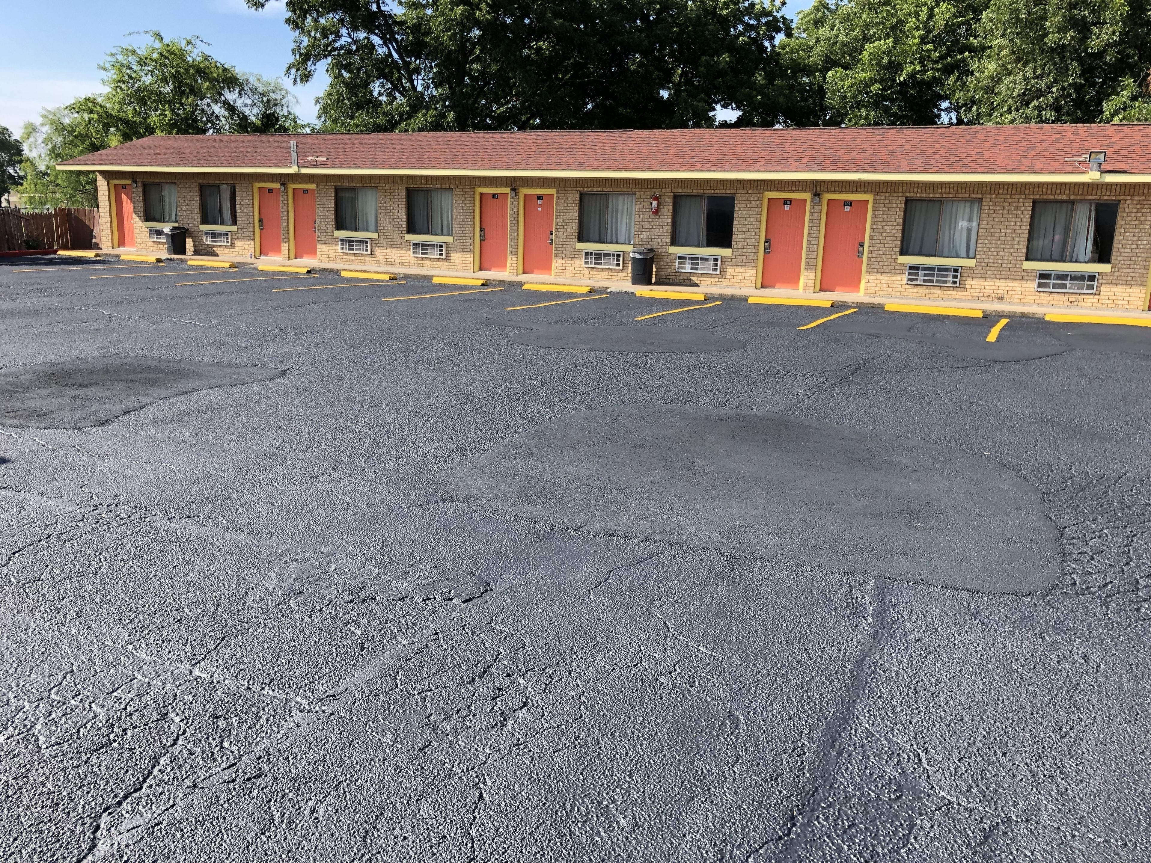 Un motel avec une rangée de chambres, chacune dotée d’une porte rouge et d’une fenêtre. Le parking est asphalté et les places sont délimitées par des lignes jaunes.