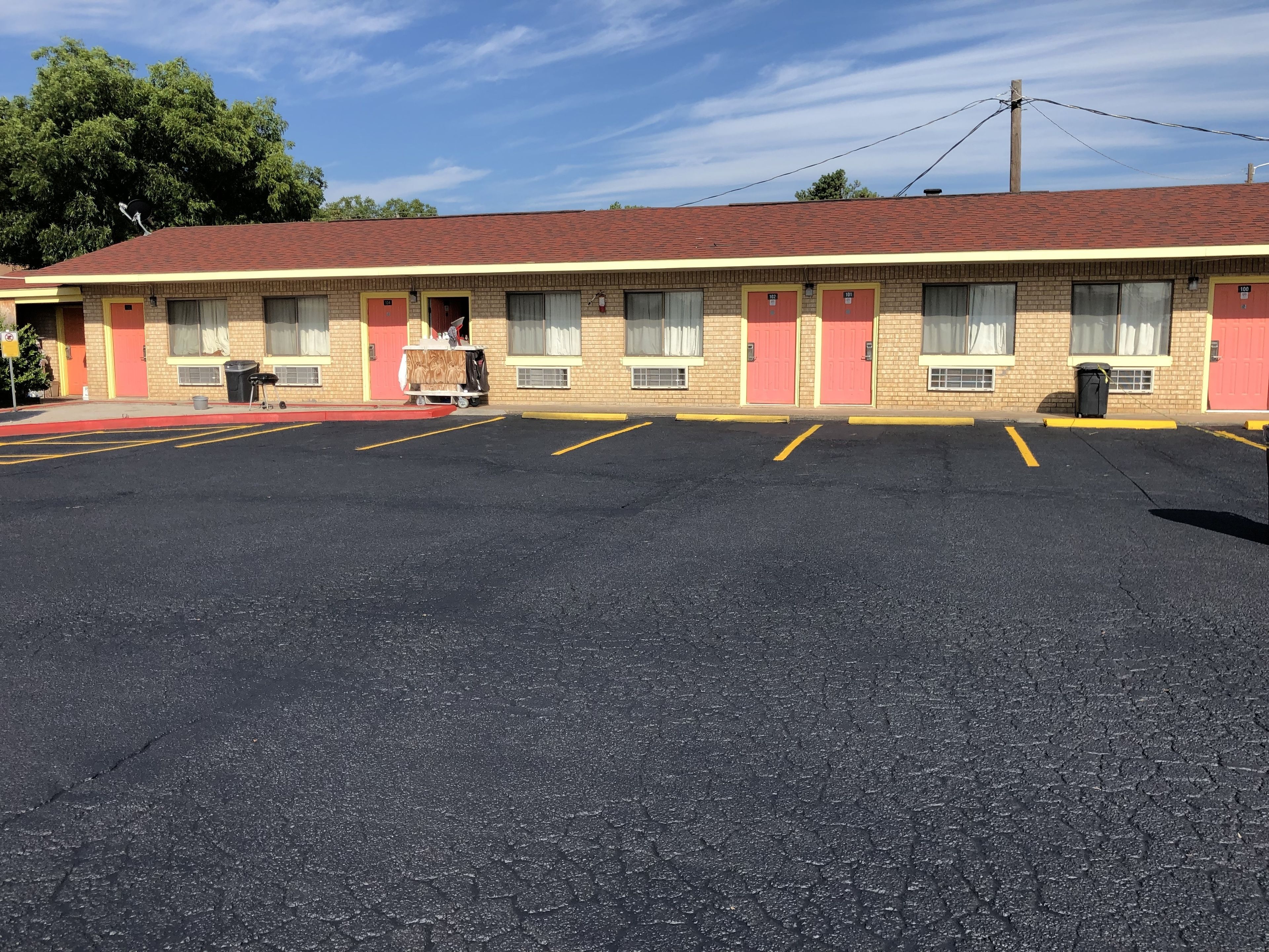 Un motel con techo rojo y detalles amarillos, que muestra una fila de habitaciones con ventanas y un estacionamiento al frente.