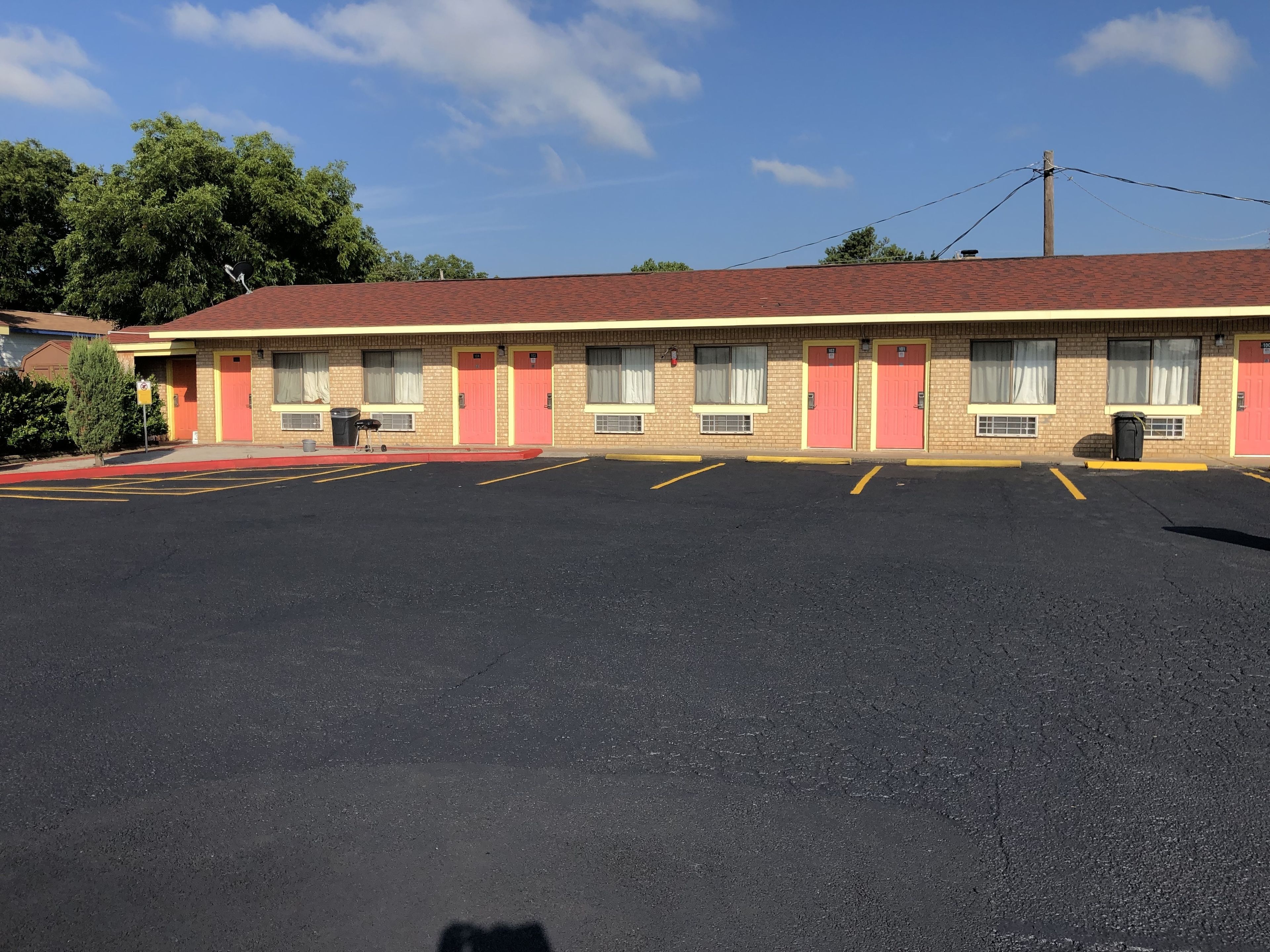 A motel with a red roof, multiple doors, and a parking lot.