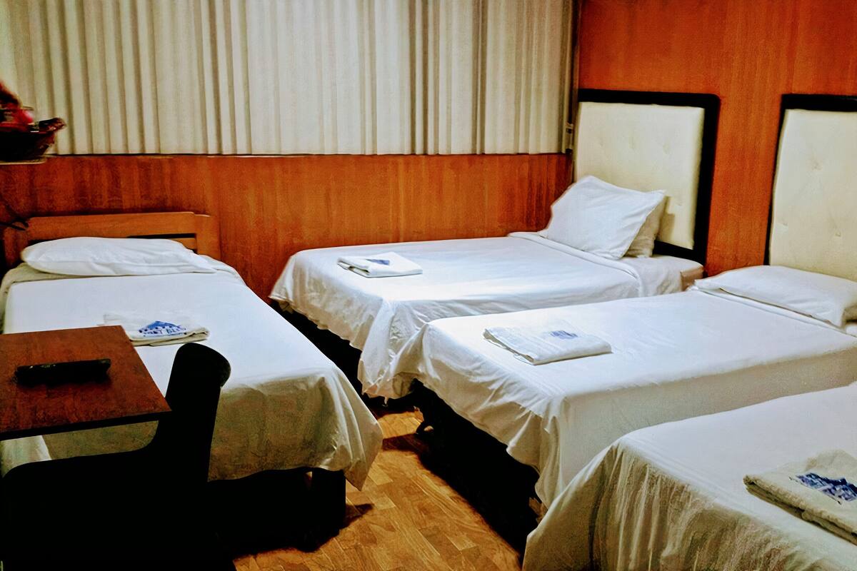 A hotel room with three single beds, a wooden headboard, a small desk, and a chair.