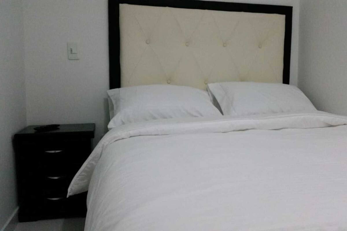 A simple, clean room with a bed, a nightstand, and a wall socket.