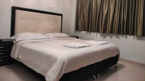 A neatly made bed with a tufted headboard, a bedside table, and a window with curtains. - Hotel Mont Bleu (Bogotá)