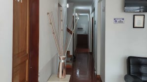 A hallway with a wooden door labeled '101', a white vase with sticks, a black leather chair, and a mounted television. - Hotel Mont Bleu (Bogotá)