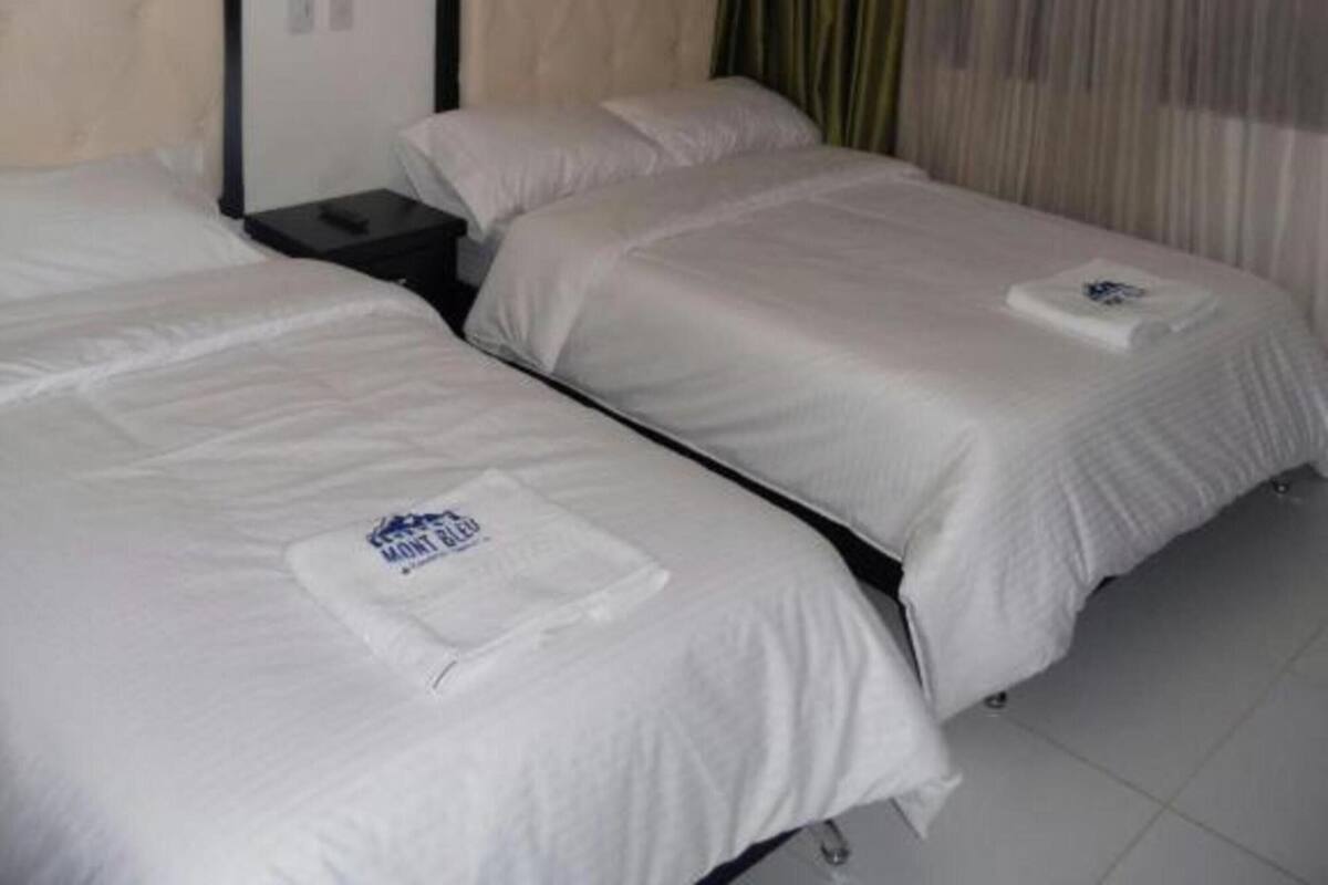 A hotel room with two single beds, a nightstand, a chandelier, and a window with curtains.