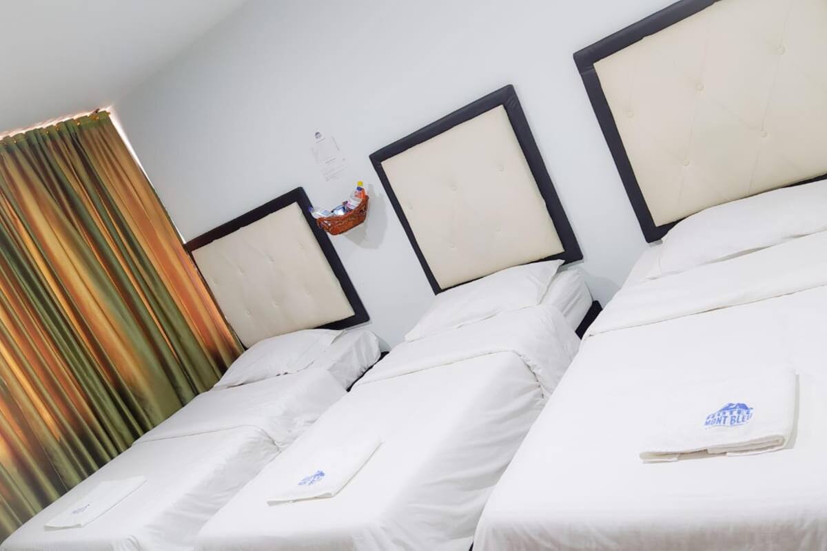 A hotel room with two single beds, a headboard, a curtain, and a small table with a bottle.