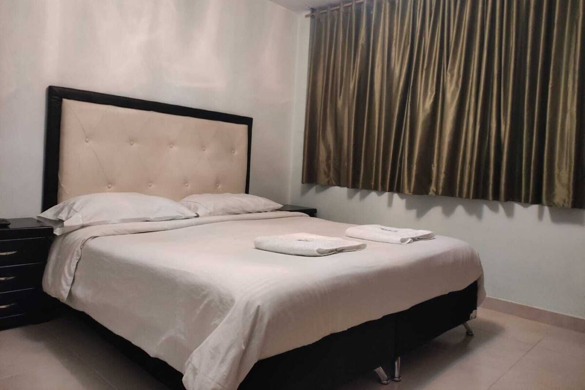 A neatly made bed with white linens, a dark headboard, and a bedside table with a lamp.