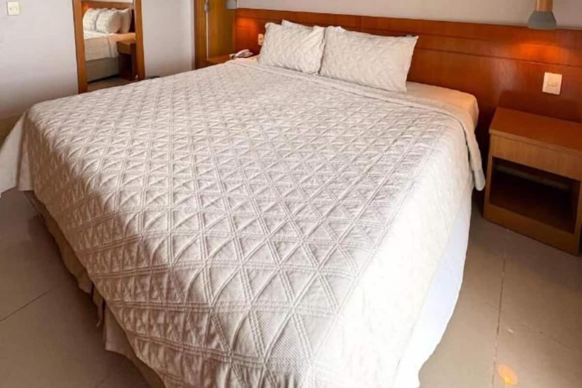 A large bed with a quilted headboard, a bedside table, and a hanging light fixture.