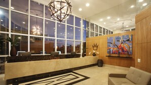 A hotel reception area with a marble counter, a sofa, and a large window with a view. - Royal Urban Macaé Hotel (Macaé)