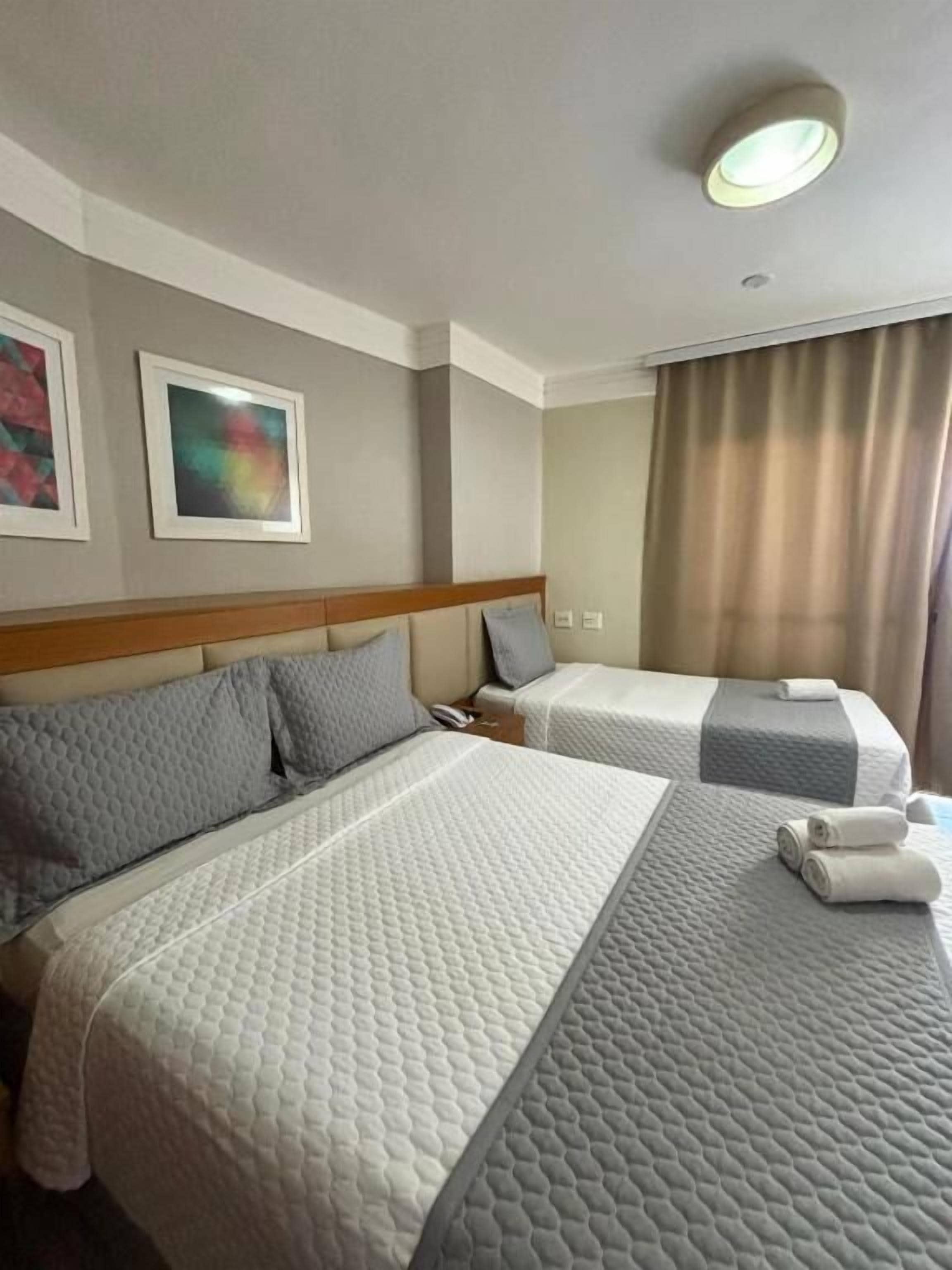 A hotel room with two beds, a headboard, a mirror, and a ceiling light.